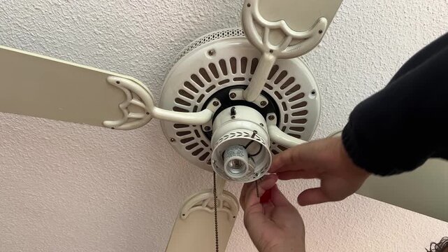 A person fine-tunes the blades and fixture of a ceiling fan, focusing on home maintenance tasks. Useful for DIY tutorials or home improvement content.