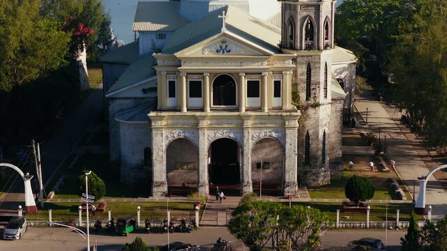 Dauis Church facade and historic bell tower in tropical Bohol town, drone ascend tilt down