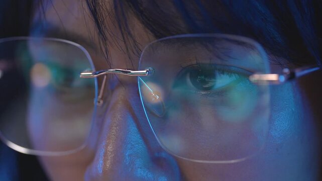 Extreme macro close up of rimless eyeglasses on Asian female programmer with bright digital programming code lines clearly reflecting on the smooth transparent lenses
