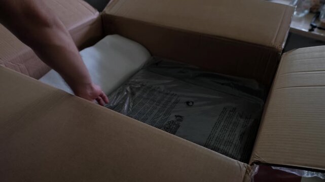 Medium shot of hands removing packaged chair parts from an opened cardboard box during indoor furniture unboxing