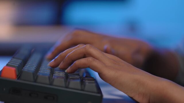 Close up shot of young Asian woman programmer hands quickly typing program code on a black mechanical computer keyboard inside a dark blue lit modern office workspace