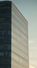 Fototapeta premium Modern Glass Skyscraper: A contemporary glass office building stands tall against a serene sky, its sleek facade reflecting the soft light of dawn, symbolizing progress and urban development.