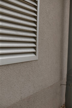 Vent and downspout meeting stucco seam, vertical composition highlights service access, textured wall surface, subtle dirt streaks, practical urban maintenance