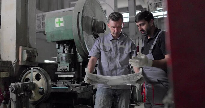 Factory Technicians Reviewing Blueprint During Machine Inspection in Metal Workshop
