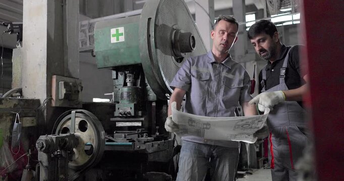 Factory Technicians Reviewing Blueprint During Machine Inspection in Metal Workshop