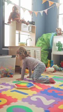 Girl kneeling on a colorful foam playmat playing with blocks near a toybox and play kitchen under bunting in a playroom; joyful play.