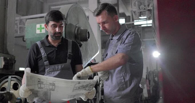 Factory Technicians Reviewing Blueprint During Machine Inspection in Metal Workshop