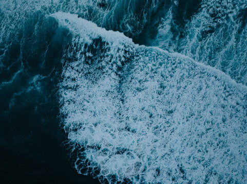 Aerial view of a powerful ocean wave breaking with white sea foam and deep blue water in San Diego, California, United States.