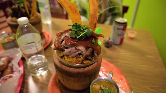 A close-up shot of a delicious mofongo dish made of mashed green plantains, garlic, and chicharron, served in a traditional wooden mortar and pestle at a restaurant.