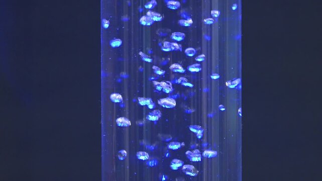Macro view of glowing hydrogen bubbles moving through vertical transparent chamber during electrolysis based renewable energy research in laboratory environment