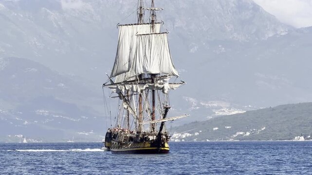 The frigate Shtandart, a replica of an 18th-century sailing ship, cruises on the calm blue waters of Montenegro with mountains in the background