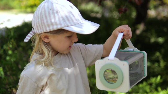 Young naturalist carefully observing insects inside a bug catching kit in a sunlit garden. Educational outdoor activity teaching a curious child about entomology and the natural world