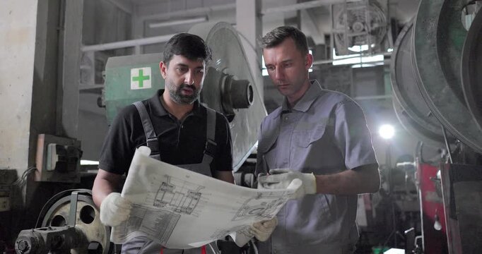 Factory Technicians Reviewing Blueprint During Machine Inspection in Metal Workshop