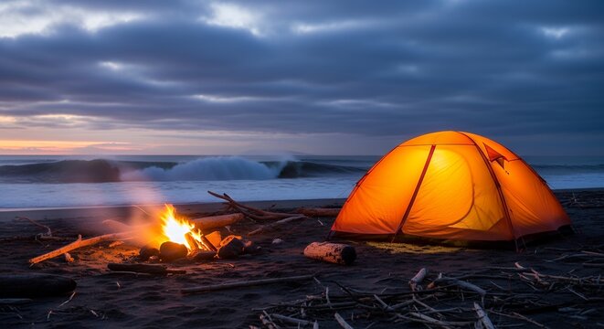 Orange camping tent illuminated by firelight on beach at dusk