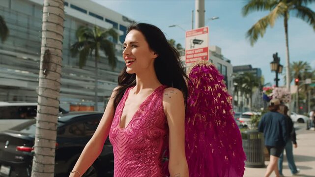 A woman dressed as a Valentine-themed angel in a vibrant pink costume walks through the luxury shopping streets of Beverly Hills holding a handmade Valentine&rsquo;s Day sign. Surrounded by palm trees