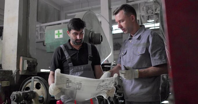 Factory Technicians Reviewing Blueprint During Machine Inspection in Metal Workshop