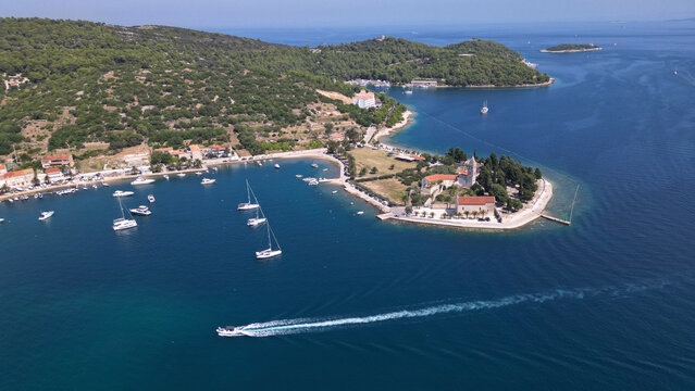 Aerial view of the Prirovo Franciscan Monastery on a peninsula with sailing boats in the bay and lush green hills Vis, Split-Dalmatia County, Croatia.