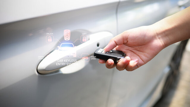 Hand holding a car key fob near a silver car door handle with translucent car keyless entry system icons overlayed, modern close-up view.