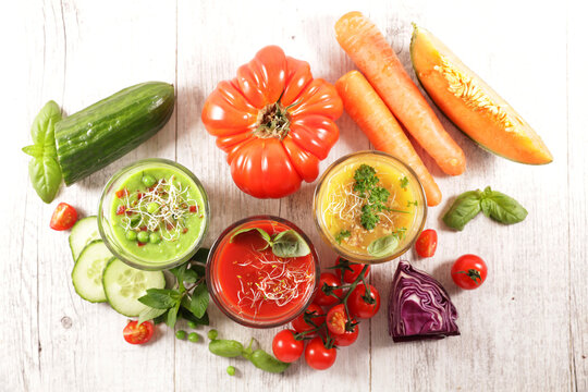 Top view of assorted fresh cold vegetable soups and raw ingredients on white wooden table