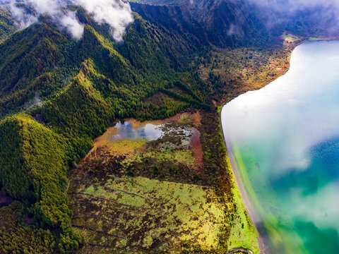 Aerial view of Lagoa do Fogo crater lake surrounded by lush green volcanic ridges and soft white clouds Agua de Alto, Azores, Portugal.