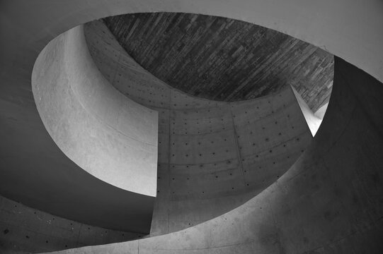 Minimalist black-and-white photo of a spiral concrete interior featuring a sweeping curved ramp and circular skylight, highlighting geometric shapes, textures, light and shadow for modern