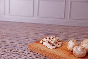 Fototapeta premium Fresh champignon mushrooms sit on a rustic wooden board. Sliced pieces rest beside whole caps, softly lit. Wooden surface shows aged grain and texture. Natural, wholesome, and simple. Ideal for health