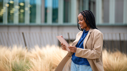 Young black businesswoman smiling holding digital tablet outdoors © Miquel