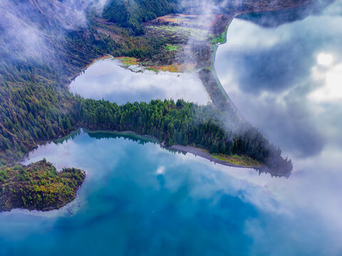 Aerial view of Lagoa do Fogo surrounded by lush green volcanic slopes and misty clouds reflecting on the turquoise water in Agua de Alto, Azores, Portugal.