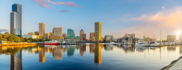 View of the downtown Baltimore skyline perfectly reflecting across the calm waters of the Inner Harbor during a golden summer sunrise in Maryland © f11photo