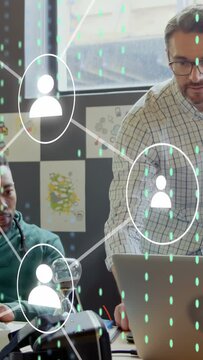 Vertical video: Standing man tapping laptop, UI icons and dashes filling while two men working tech