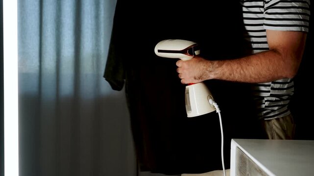 Man uses portable garment steamer to smooth wrinkles from black t-shirt