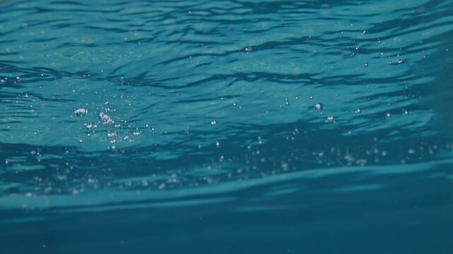 Suspended air bubbles drift beneath rippled tropical Atlantic surface water super slow motion underwater shot with soft refracted light patterns.