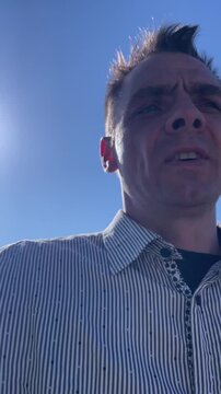Outdoor man shouts at camera. Person passionately yells during bright sunlight. Individual vocally expressing strong opinions outside in sunlight