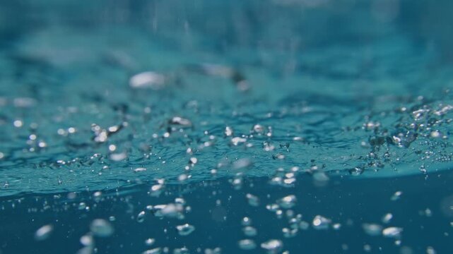 Bubble turbulence drifts beneath tropical Atlantic surface ripples super slow motion underwater shot with suspended microbubbles and refracted blue light.