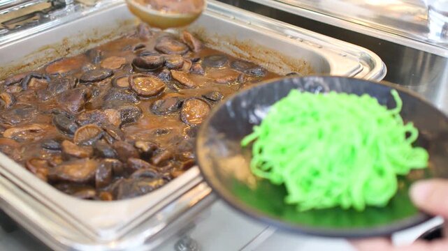 Server Scooping Shiitake Mushrooms from Chafing Dish onto Jade Noodles