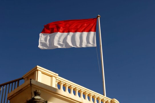 National flag of Monaco waving on a flagpole in Monte Carlo with trees and buildings in background