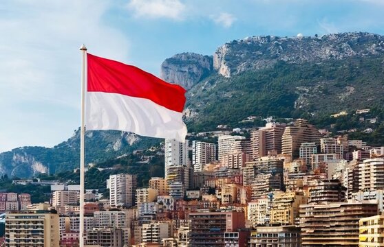 National flag of Monaco waving on a flagpole in Monte Carlo with trees and buildings in background