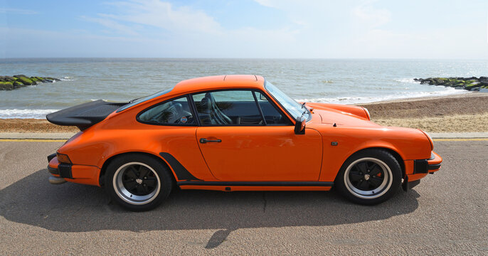 Classic Porsche 911 Turbo parked on seafront promenade beach and sea in background