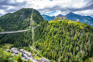 Fototapeta premium A suspension bridge connects the hillside to the ruins of Ehrenberg Castle. The Schlosskopf fortress stands above. Visitors can explore the area surrounded by mountains and trees.