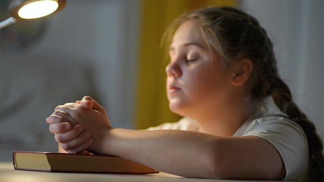 Child sits at table with head bowed, praying deeply. Girl devotion clear through posture and still hands. Hope lies in silence. Girl praying over bible reflects devotion, girl devotion shows hope