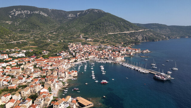 Aerial view of the coastal town of Komiza with its harbor full of boats and red-roofed houses nestled against green mountains Komiza, Split-Dalmatia County, Croatia.
