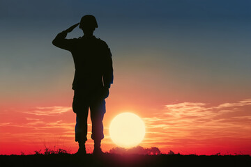 Fototapeta premium Silhouette of soldier salutes at sunset. Sunset colors paint sky in warm hues. Soldier stands firm on horizon line. His posture shows respect and honor. moment captures military duty