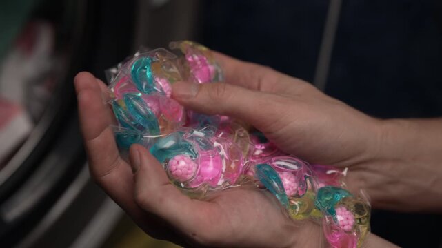 Male hands holding large handful of colorful laundry gel capsules with concentrated cleaning power. Modern household chore concept showing convenient, pre measured liquid detergent pods, slow motion.
