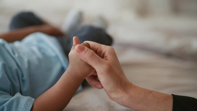 Tenderness and love in family, mother stroking hand of her infant son, closeup. Enjoy time together, calmness and safety, african american woman and little child in bedroom, feel moments of happiness