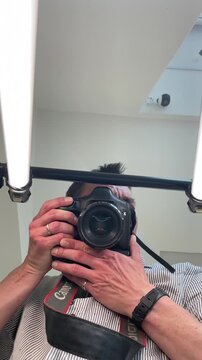 White man photographer in studio holding DSLR, shooting selfportrait, inspecting lens, adjusting lighting, testing composition for headshot, behindthescenes