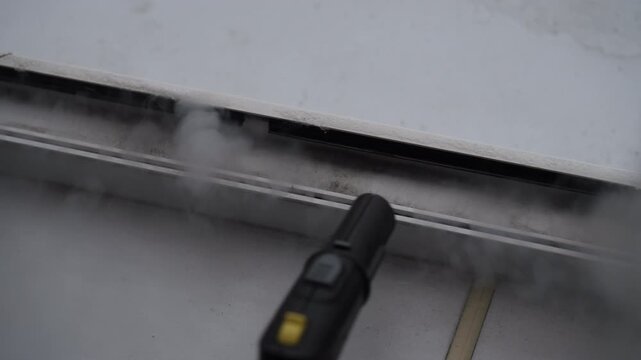 Housekeeper worker using powerful steam cleaner to remove dirt and grime from sliding tracks of modern white window frame, detailing deep cleaning process for household maintenance, slow motion.