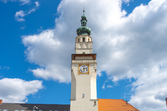 The town hall tower in Boskovice shows a clock and green dome. Clear blue sky and clouds surround the tower. The scene is part of daily life in the town.