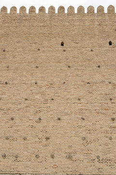 Massive brick wall of the Ark Fortress in Bukhara with crenellations and wooden scaffolding pegs. Ancient defensive architecture ideal for travel and history publications.