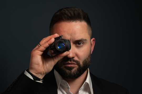 Serious professional tactical operative or security contractor holding night vision monocular to his eye looking at camera against dark background