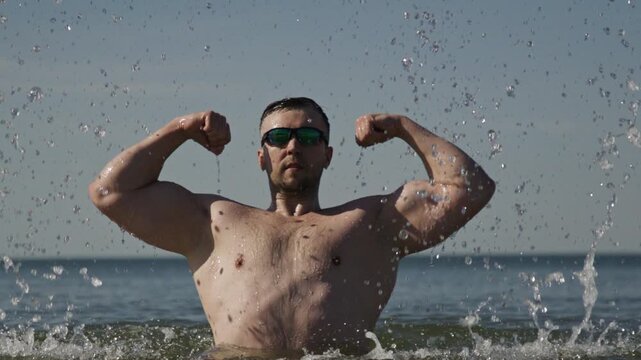 Biceps muscles highlight strong physique. Man flexing biceps on beach. Biceps training supports athletic body. Ocean splash shows biceps definition.